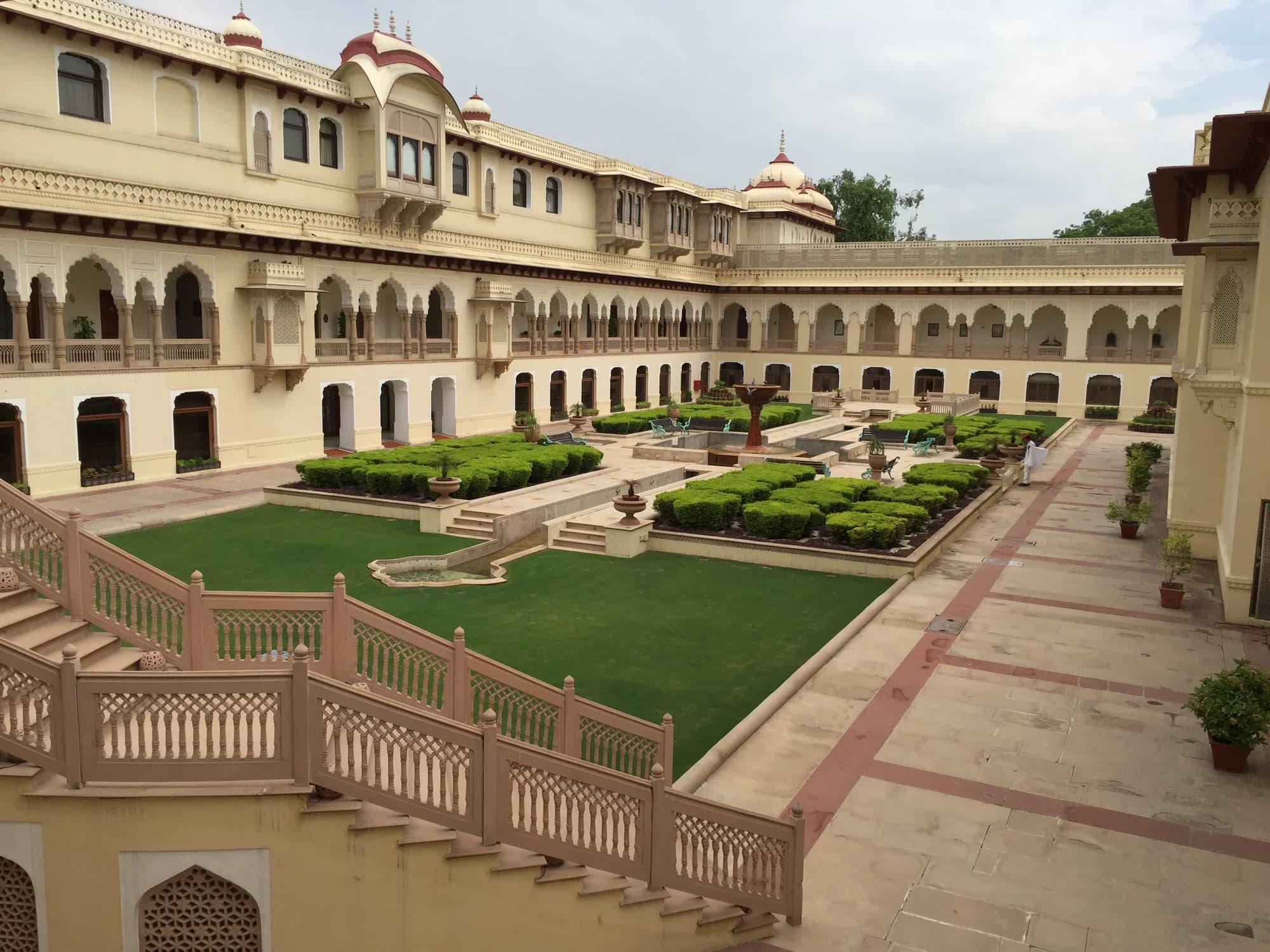 The front porch arrival at Rambagh Palace — liveried staff in cobalt-blue turbans, tuberose garlands, a vintage Bentley permanently stationed beneath the porte-cochère as a tribute to the Maharaja's automotive passion