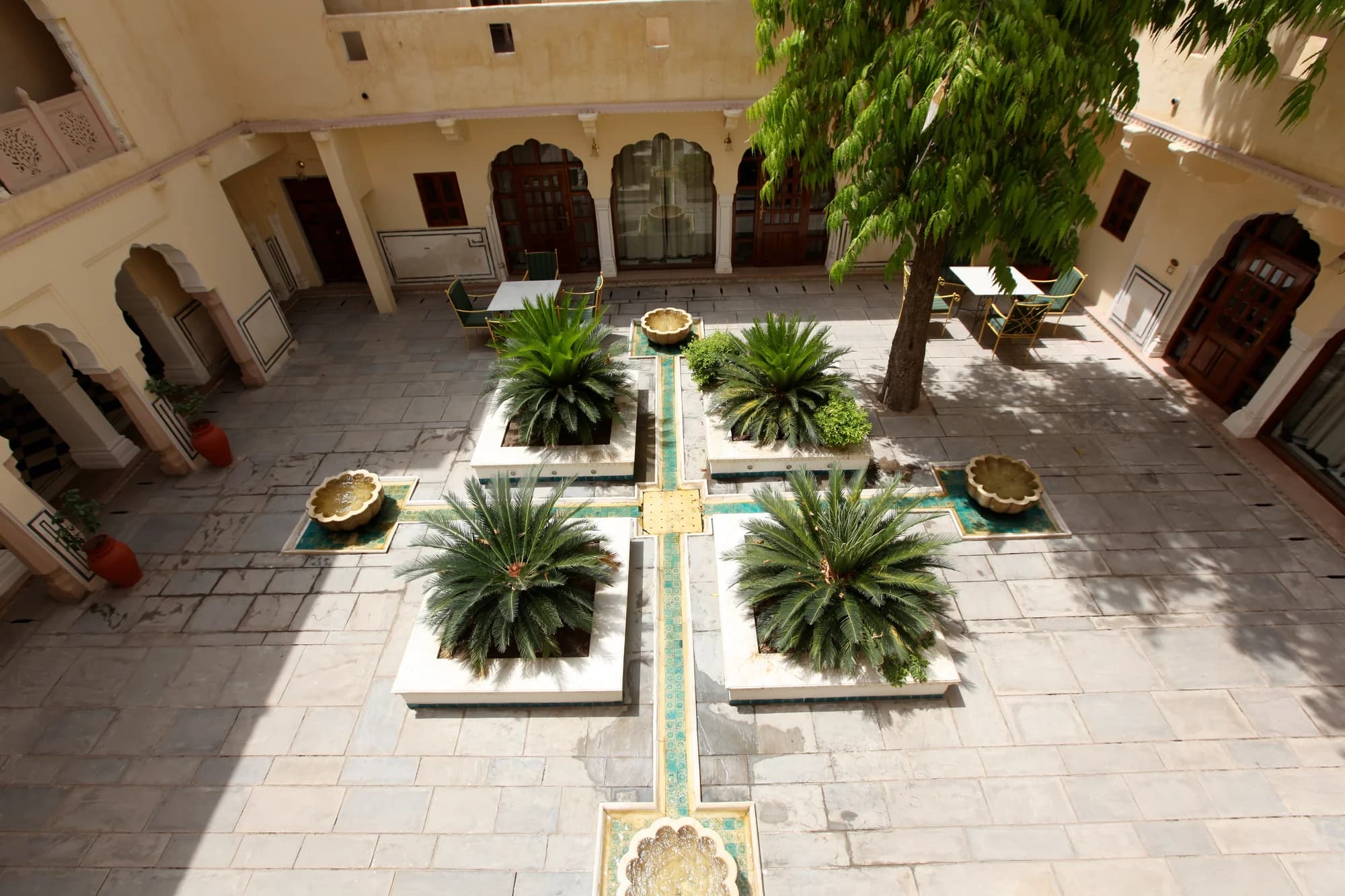 The inner courtyard of Samode Haveli — hand-painted frescoes in vegetable dyes covering every surface, their colours softened by two centuries of gentle Rajasthani sunlight, a fountain murmuring at the centre of the marble floor