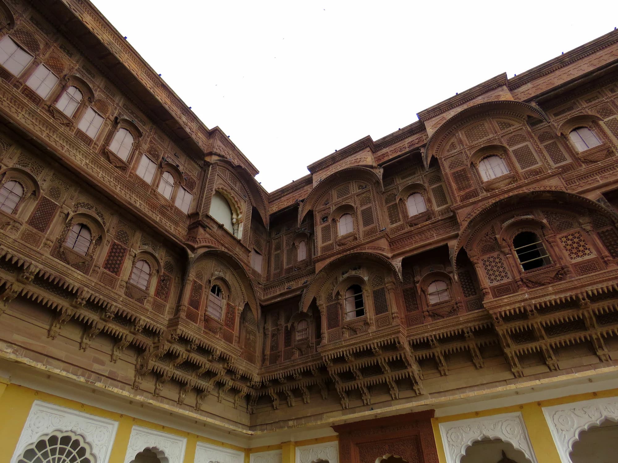 The central courtyard at Rohet Garh — neem trees casting dappled shade, a fountain murmuring at the centre, arcades lined with family photographs spanning four centuries of Champawat Rajput history