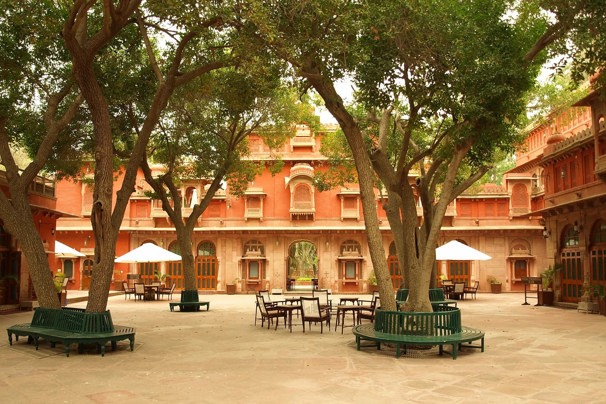 Gajner Palace at sunset — the red sandstone facade reflected in the still waters of Gajner Lake, cranes and flamingos flocking to the shore, the silence of the Thar broken only by the call of peacocks