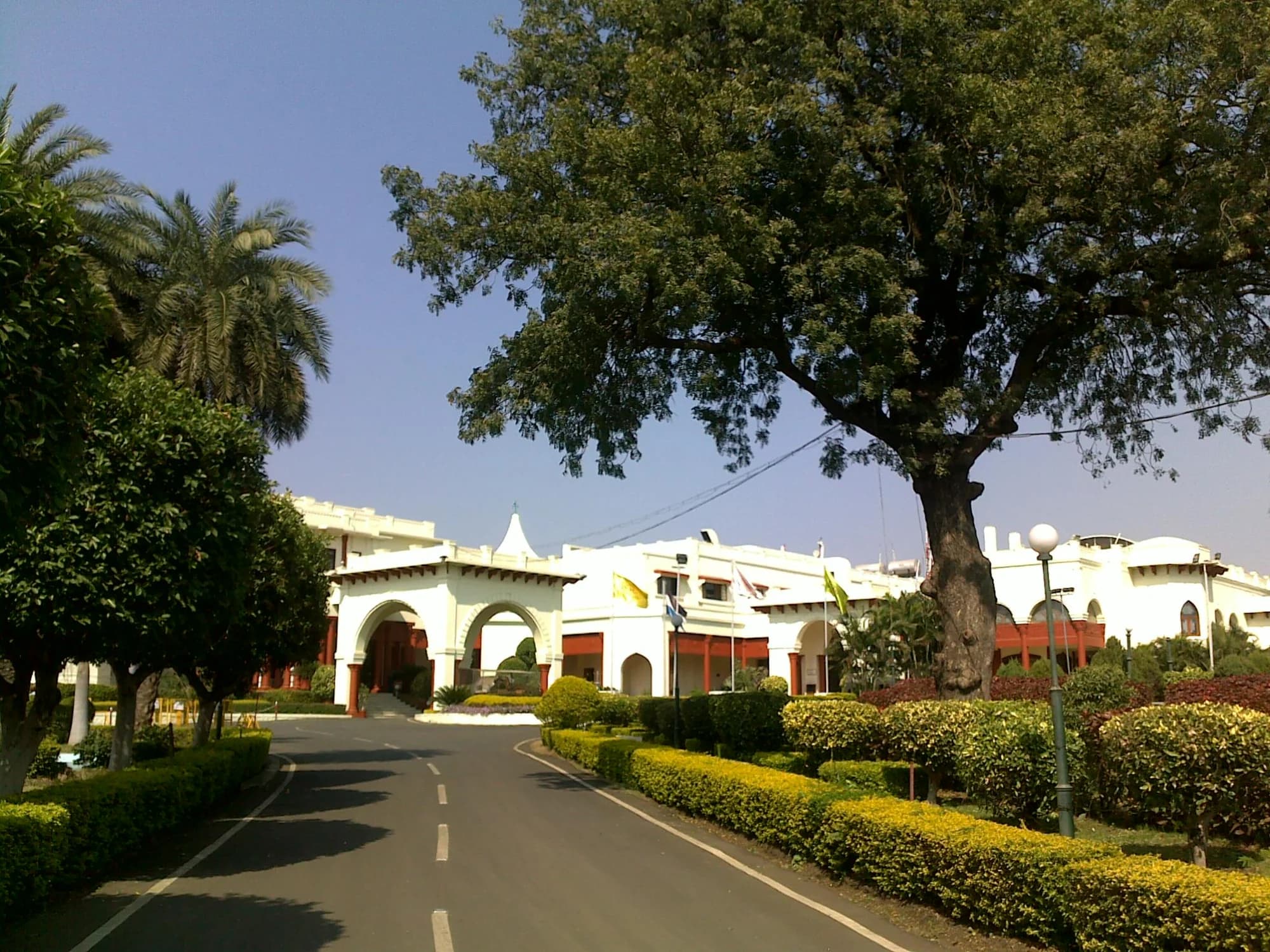 Noor-Us-Sabah Palace at dawn — the white facade catching the first light, its arches and domes glowing against the green of the surrounding hills, the lakes of Bhopal shimmering in the valley below