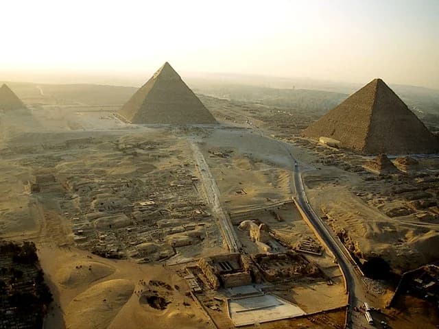 The Nile at sunset — a felucca gliding across the brown water with its lateen sail catching the evening breeze, the minarets of Islamic Cairo silhouetted against a sky of gold, rose, and deepening violet, the city a constant hum of traffic and prayer and twenty-two million lives, the river that created Egypt doing what it has done for millennia — flowing, silently, beautifully, indifferently, toward the sea